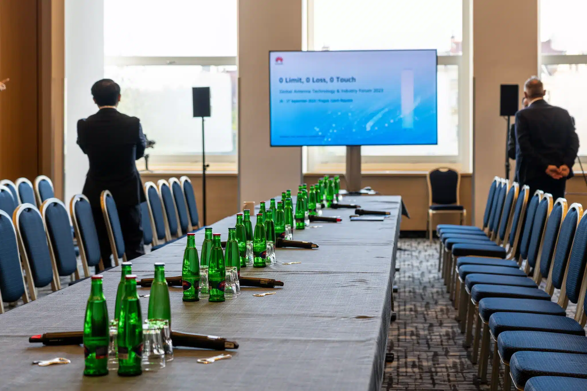 Ein Konferenztisch, bestückt mit Mikrofonen vor einem großen Bildschirm und Lautsprechern.